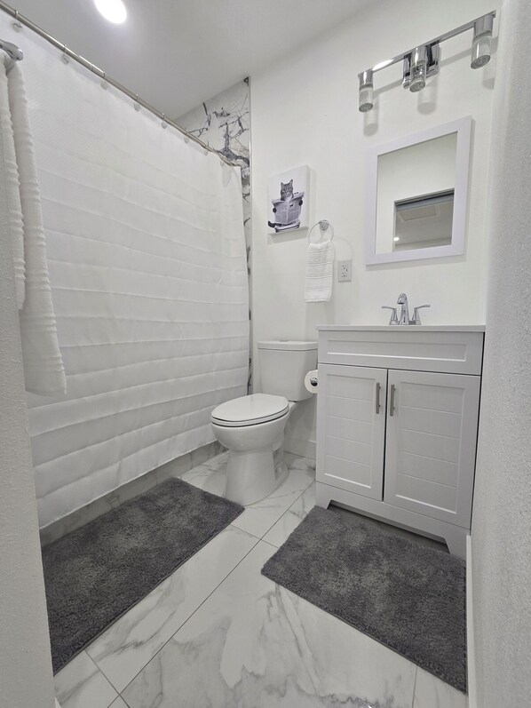 Ein Badezimmer mit Toilette, Duschvorhang, Handtuchhalter, Waschbecken mit Spiegel und Ablage.
