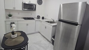 A modern kitchen with white cabinets, a stainless steel refrigerator, a microwave, and a clock on the wall.