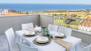 A dining table set on a balcony overlooking a coastal view with a clear sky. - Vista Blu by Interhome (Valledoria)
