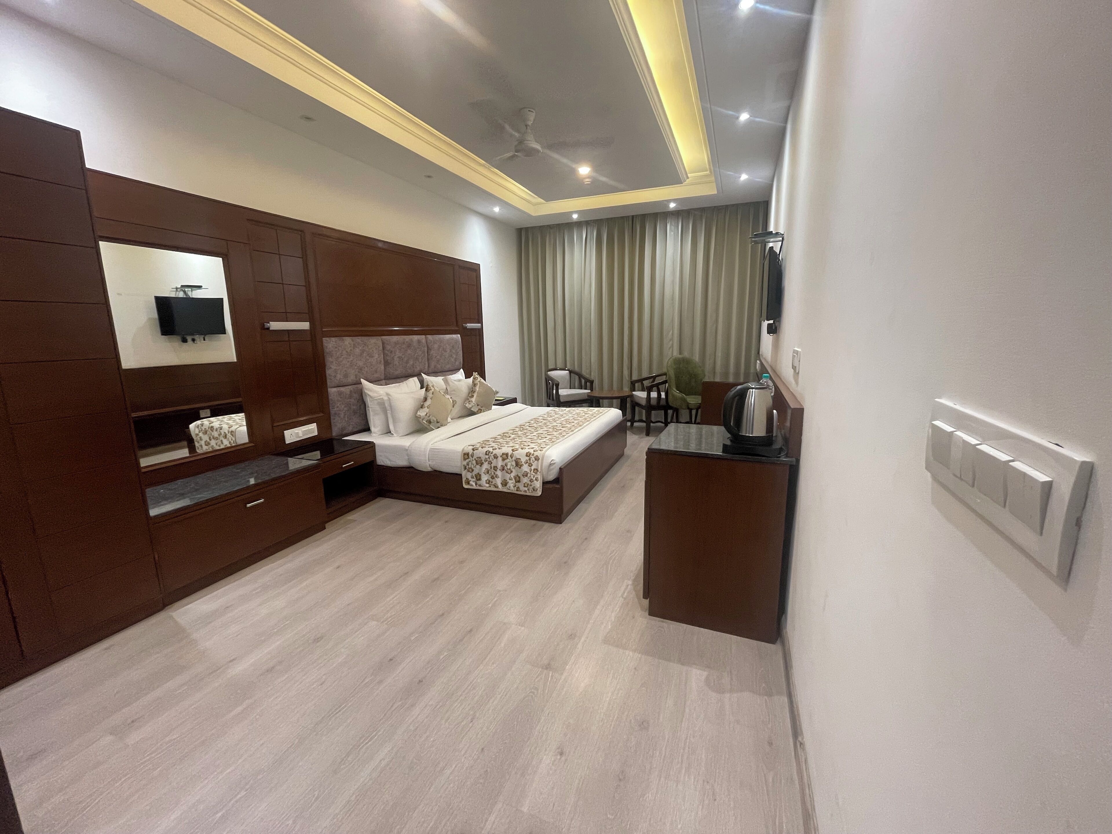 A modern hotel room with a large bed, a TV mounted on the wall, a desk with a kettle, and a ceiling fan.
