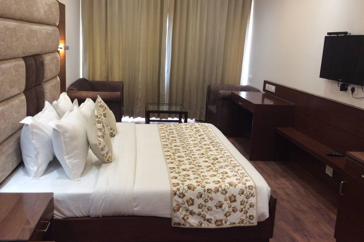 Quarto de hotel com uma cama grande, uma escrivaninha, uma cadeira, uma televisão e uma janela com cortinas.