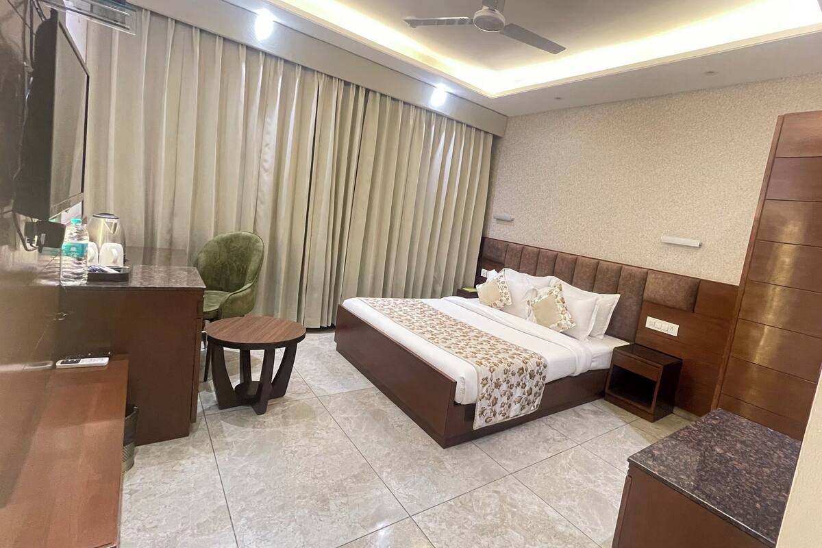 Quarto de hotel com cama, mesa de cabeceira, cadeira e escrivaninha, com garrafa de água e copos.