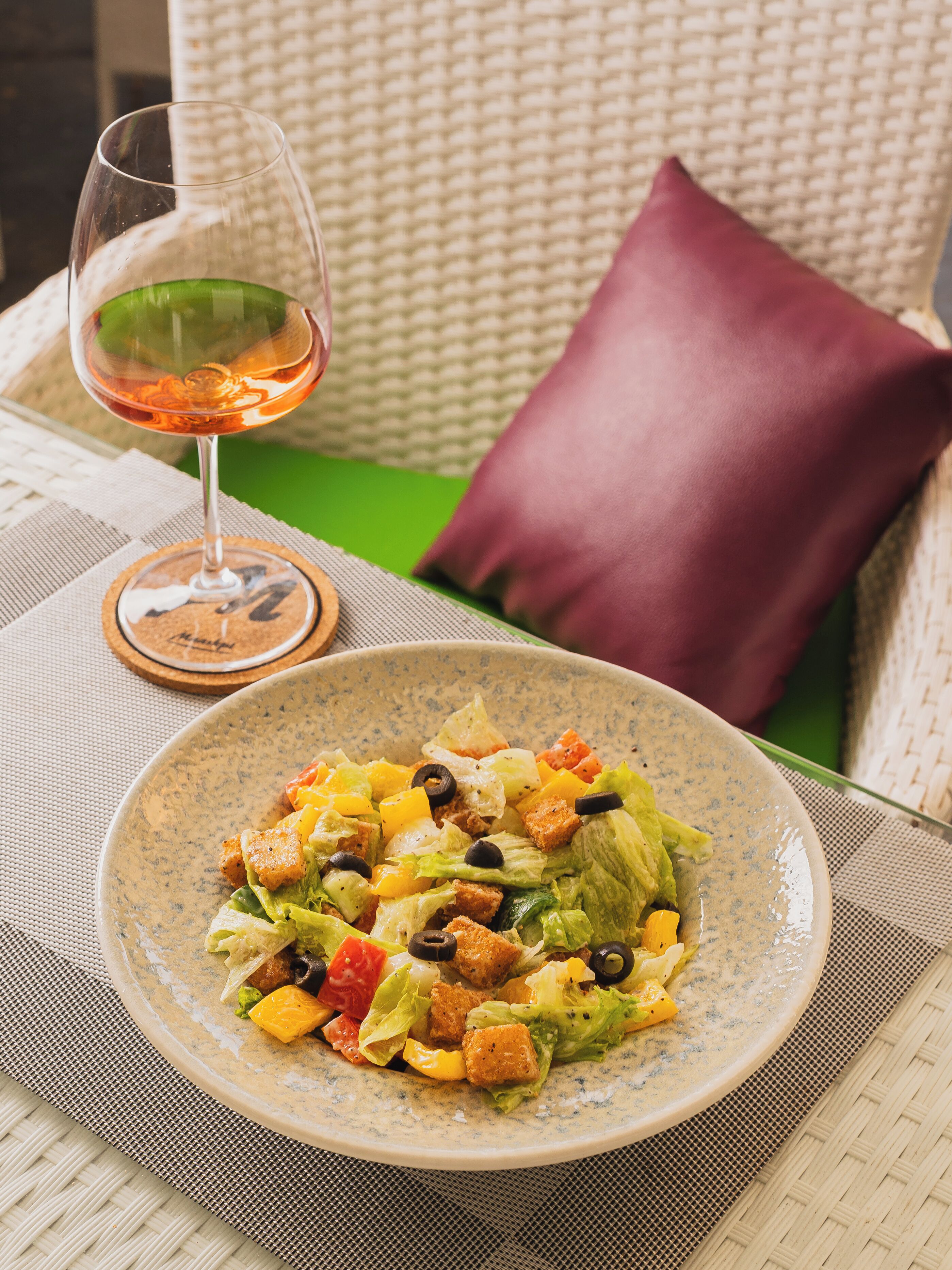 A dining table with a plate of salad, a glass of wine, and a cushion.