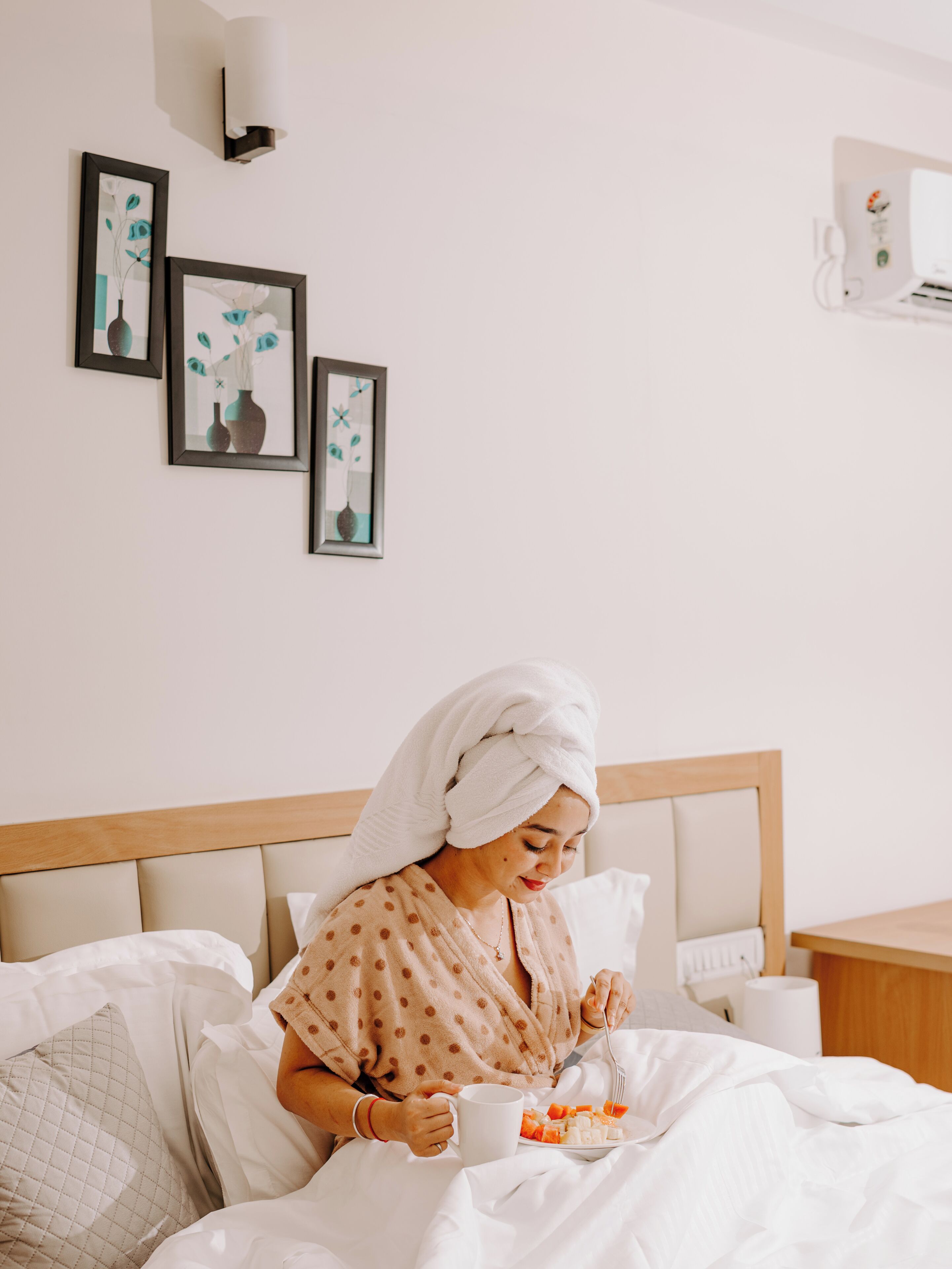 A hotel room with a bed, a bedside table, a wall-mounted lamp, and framed artwork on the wall.