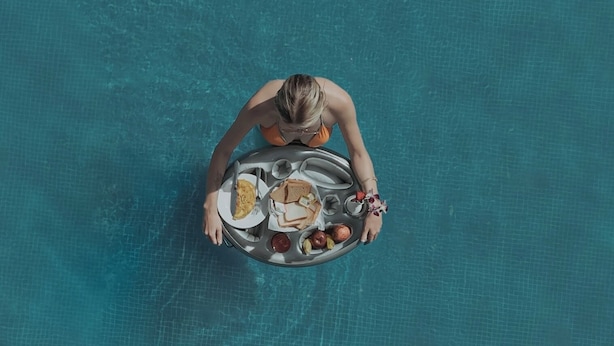 Une personne dans une piscine, tenant un plateau rempli de différents aliments.