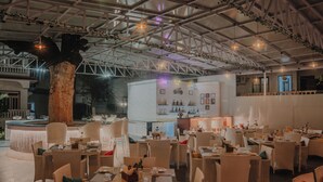 Un espace de restauration intérieur aménagé avec des meubles en osier, un bar central et un plafond avec des poutres apparentes et des luminaires suspendus.