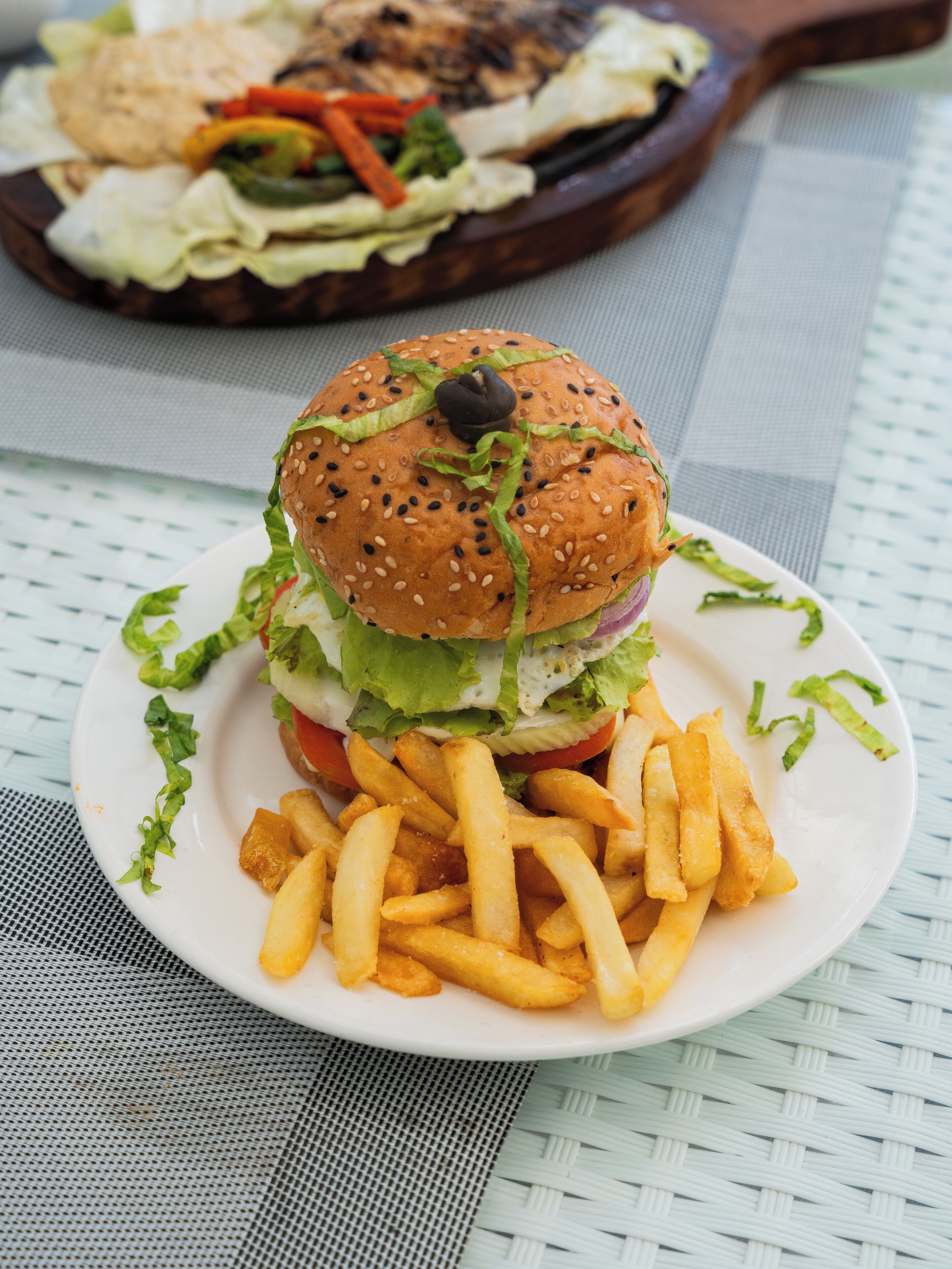 A plate with a burger and fries on a woven tablecloth.