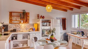 A compact kitchen with a wooden ceiling, a built-in microwave, a refrigerator, and a dining area with a glass table and chairs. - Cozy House w/ BBQ, Teide Views, Near Town (Icod de los Vinos)