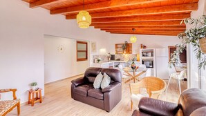 A living room with a brown leather sofa, a dining table with chairs, a kitchen area with a refrigerator, and a wooden ceiling. - Cozy House w/ BBQ, Teide Views, Near Town (Icod de los Vinos)
