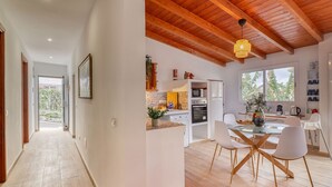 A modern kitchen with white cabinetry, a dining area with a glass table and white chairs, and a wooden ceiling. - Cozy House w/ BBQ, Teide Views, Near Town (Icod de los Vinos)