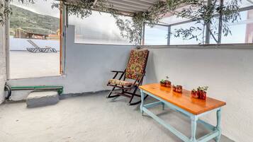 Un patio techado con una mecedora, una mesa de madera y plantas en macetas.