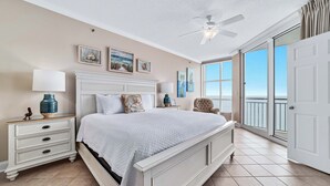 Een slaapkamer met een bed, nachtkastjes, een plafondventilator en uitzicht op de oceaan door grote ramen.