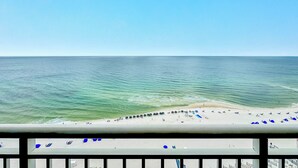 Uitzicht op een strand vanaf een balkon met een balustrade, heldere lucht en een kalme zee.