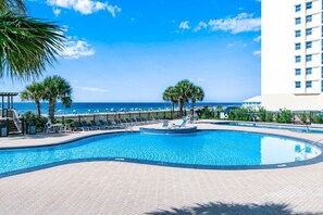 Ein Swimmingpool mit Liegestühlen und Palmen, mit Blick auf den Ozean.