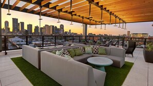 Un salón en la azotea con vista al horizonte urbano, techo de madera y zona de césped artificial verde.