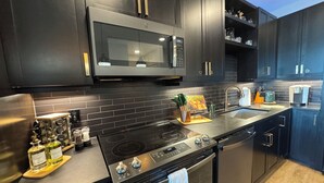 Una cocina moderna con armarios oscuros, estufa de acero inoxidable, microondas y horno empotrado.