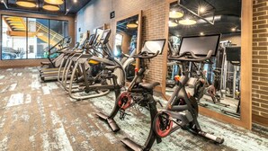 Un gimnasio con bicicletas estáticas, espejos y una pared de ladrillo.