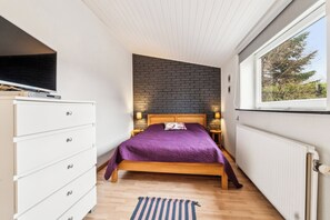 A bedroom with a bed, a dresser, a TV, a window, and a brick wall. - Cozy holiday home with lots of charm (Aakirkeby)