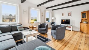 Uma sala de estar moderna com um sofá, poltronas, uma TV e piso de madeira.