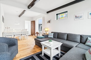 Una sala de estar moderna con un sofá gris, una mesa de centro blanca y un comedor con una mesa y sillas blancas.