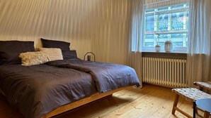 A bedroom with a bed, a window with curtains, a radiator, and a small table. - Tante Hedwig - cozy vacation apartment in Rodalben close to the rock hiking trail (Rodalben)