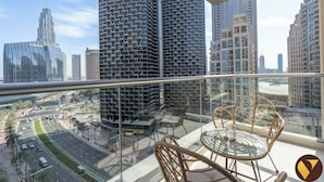 A balcony with a glass table and wicker chairs, overlooking a cityscape with modern high-rise buildings.