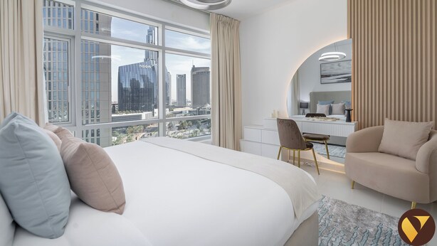 A modern hotel room with a large bed, a desk, and a view of the cityscape.