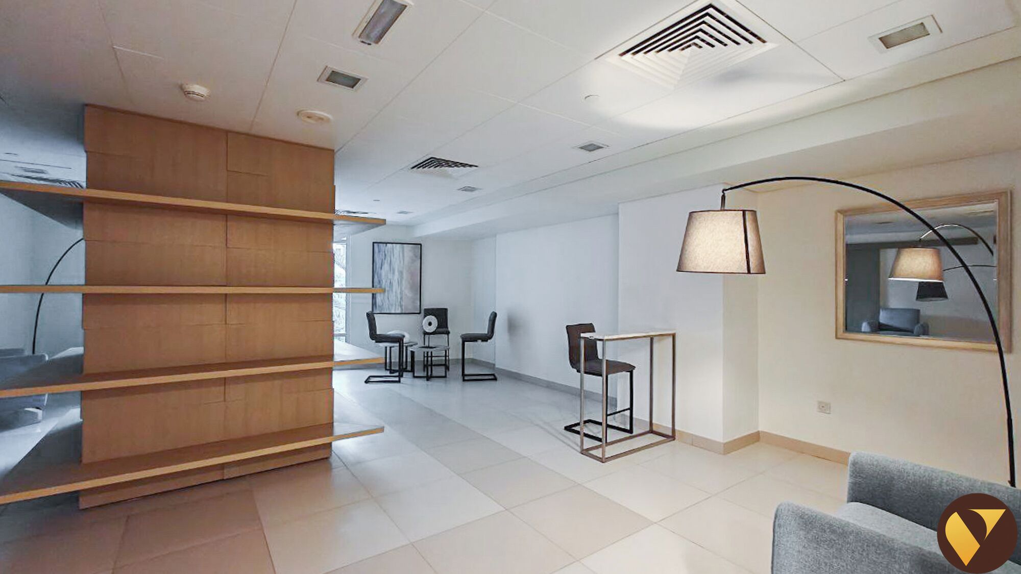 Een moderne hotelkamer met een houten boekenkast, een bureau met stoel, een bijzettafeltje met lamp en een grote spiegel.
