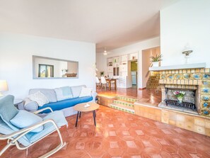 Una sala de estar con un sofá, una silla, una mesita, una chimenea y una cocina al fondo.