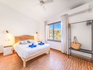 Un dormitorio con cama, ventana con vistas, ventilador de techo y mesita de noche.