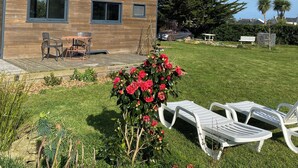 A modern house with a wooden exterior, a deck, and a garden with red flowers and white lounge chairs. - Walk to the beach for ker Ael's Tiny house (Landéda)