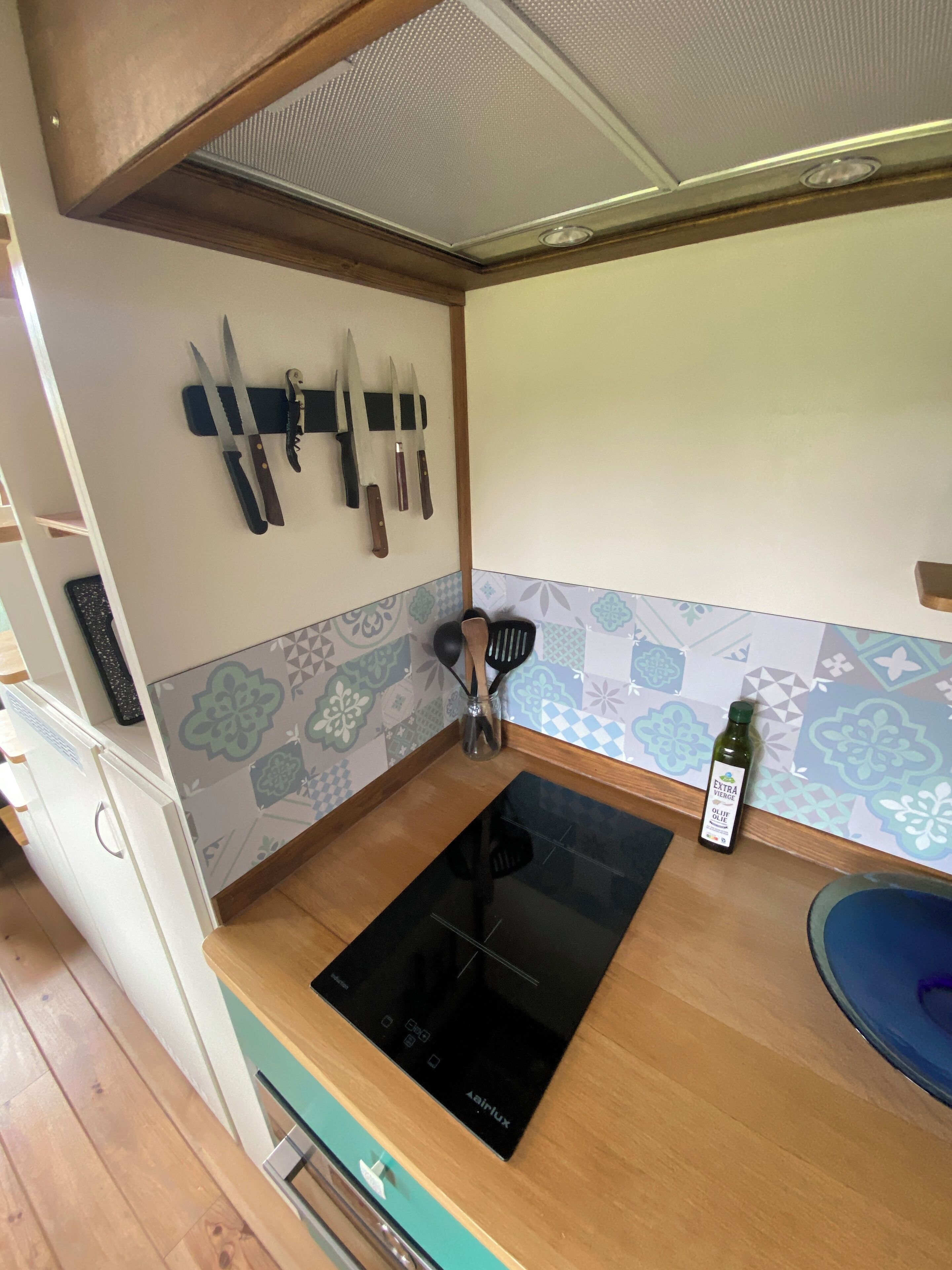 A compact kitchen with a black induction cooktop, a small sink, and a knife rack on the wall.