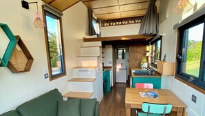 A compact living space with a green sofa, a wooden dining table with chairs, and a kitchen area. - Walk to the beach for ker Ael's Tiny house (Landéda)