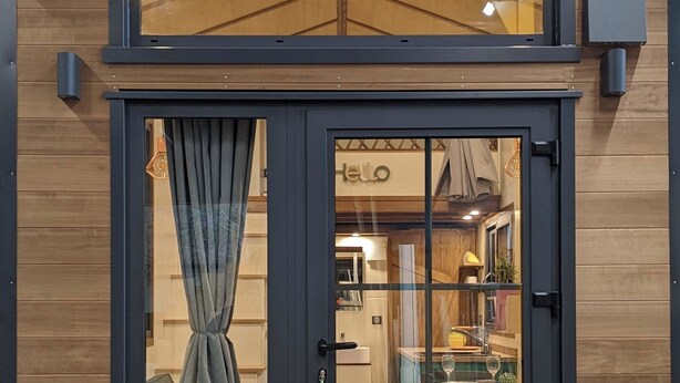 A modern wooden house with a dark grey door, a visible interior with a 'hello' sign, and a window with curtains. - Walk to the beach for ker Ael's Tiny house (Landéda)