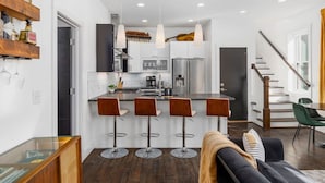 A modern kitchen with a central island, bar stools, and a staircase leading to a dining area.
