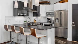 A modern kitchen with a central island, bar stools, stainless steel appliances, and pendant lighting.