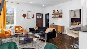 A modern living room with a black sofa, orange chairs, a coffee table, and a dining area with a bar.