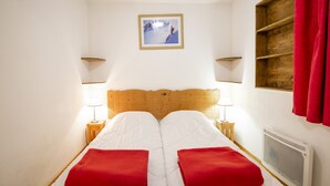A double bed with two red pillows, a wooden headboard, bedside lamps, a framed picture on the wall, and a window with a red curtain. - Holiday home for 6 people with balcony (Val Cenis)