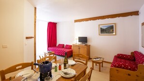 A small, cozy room with a wooden dining table, a red bed with matching pillows, a television on a wooden cabinet, and a framed picture on the wall. - Holiday home for 6 people with balcony (Val Cenis)