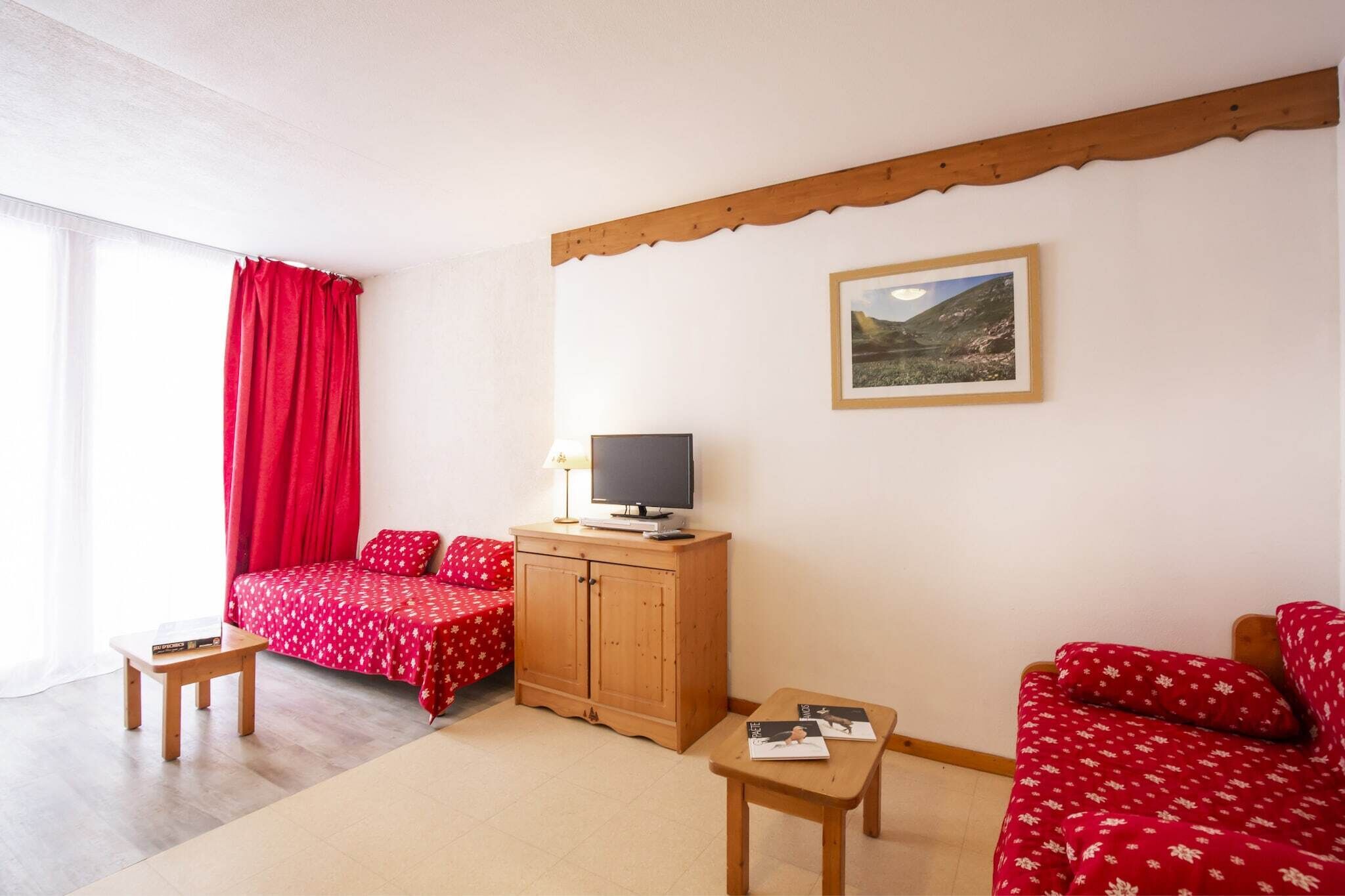 A room with a bed, a TV on a wooden cabinet, a small table, and a sofa.