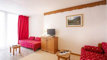 A room with a bed, a TV on a wooden cabinet, a small table, and a sofa.