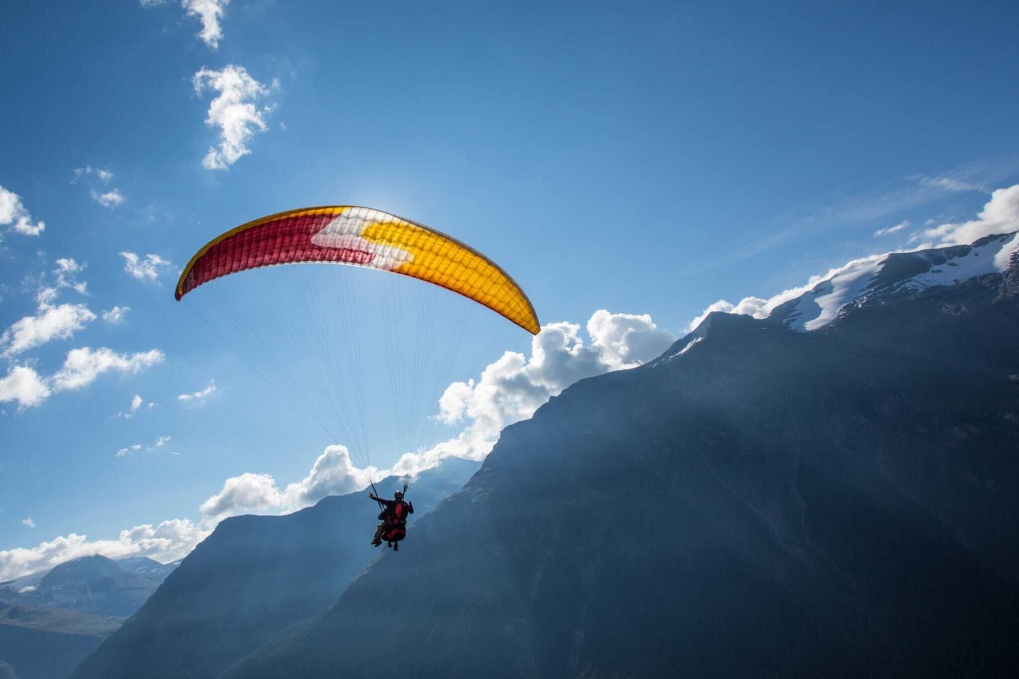 A paraglider descending towards a mountainous landscape.