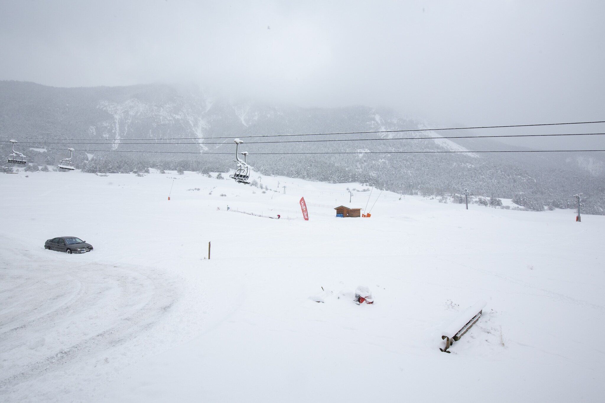 Une piste de ski enneigée, avec un télésiège, un petit chalet et une voiture.