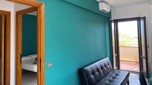 A room with teal walls, a black leather bench, a bed, and a sliding glass door leading to an outdoor area.