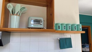 A kitchen with a wooden shelf holding a toaster, a set of utensils, and teal containers.