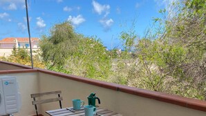 A balcony with a table and chairs, a green watering can, and a white air conditioning unit.