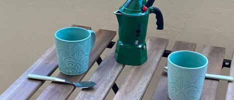 A wooden table with two turquoise patterned cups and a green manual espresso machine.