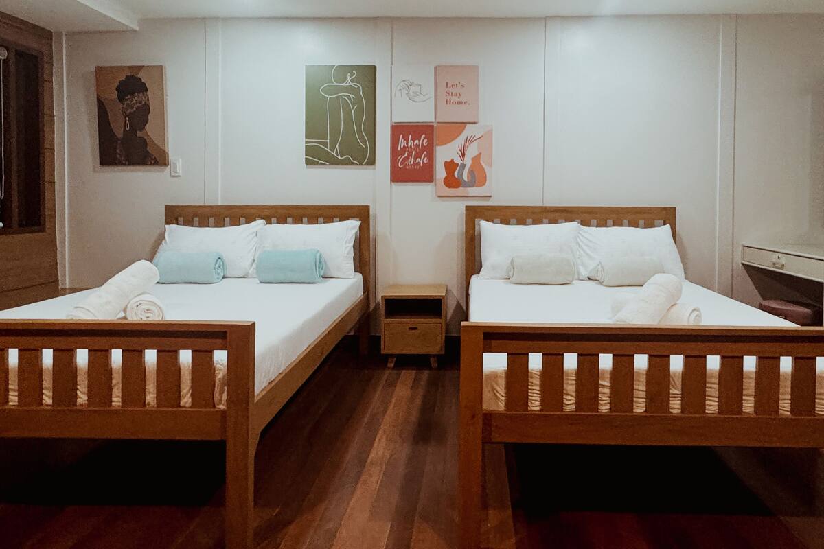 A hotel room with two wooden beds, white bedding, and a small wooden nightstand between them.