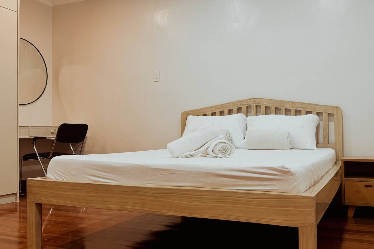 A neatly made bed with white linens and pillows, a wooden headboard, and a small wooden nightstand beside it.