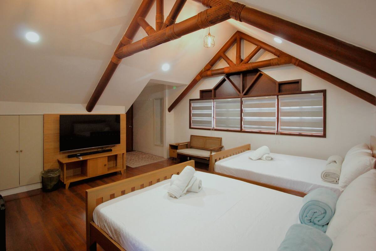 A bedroom with two beds, a TV, and wooden beams.